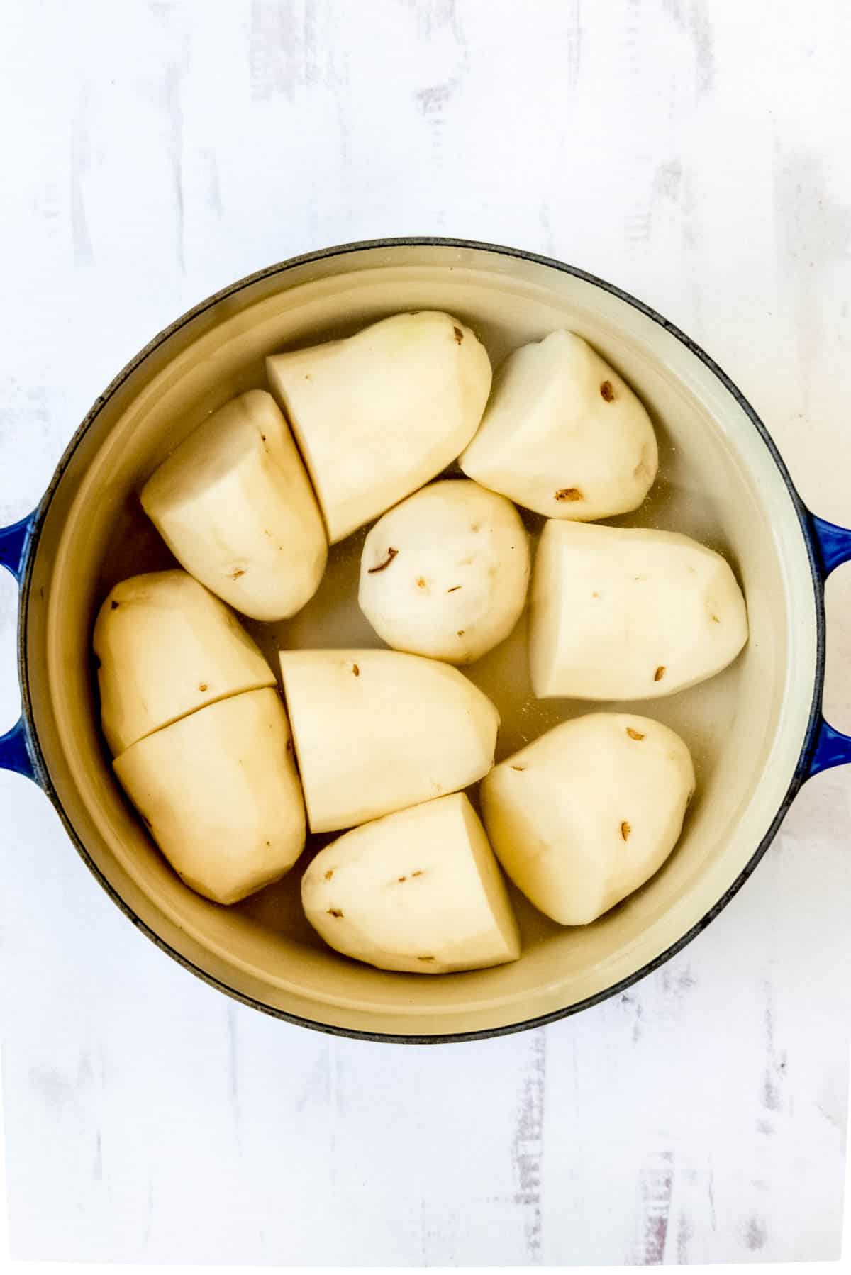 Peeled potato halves in a large pot.