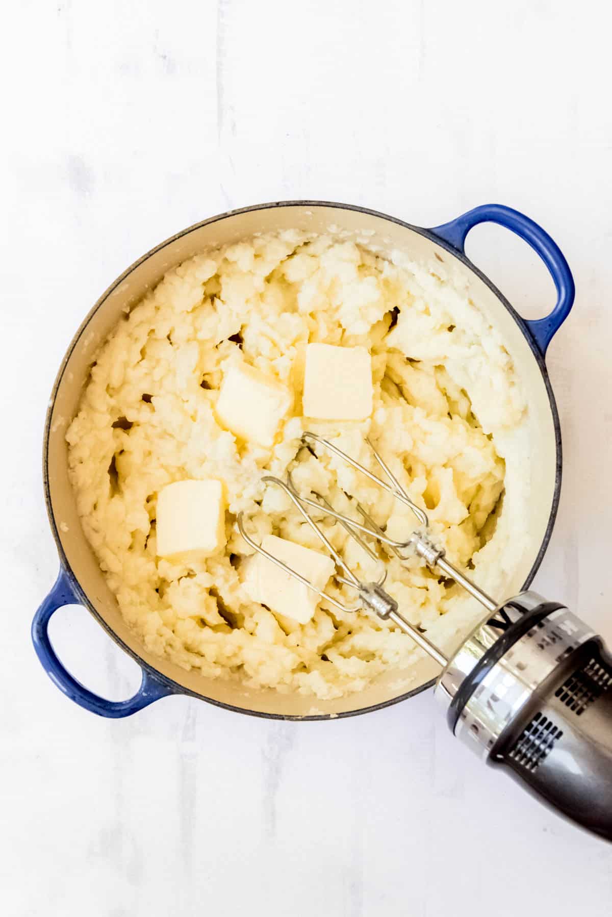 Adding softened butter to mashed potatoes in a large pot.