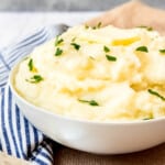 An image of a bowl of creamy mashed potatoes topped with butter and chopped parsley.