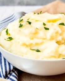 An image of a bowl of creamy mashed potatoes topped with butter and chopped parsley.