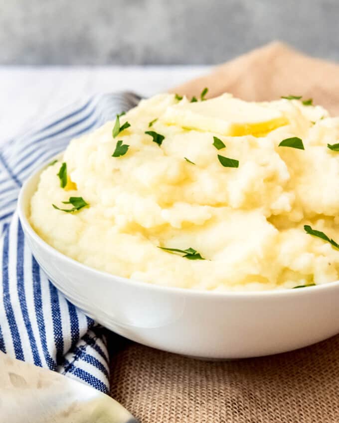 An image of a bowl of creamy mashed potatoes topped with butter and chopped parsley.