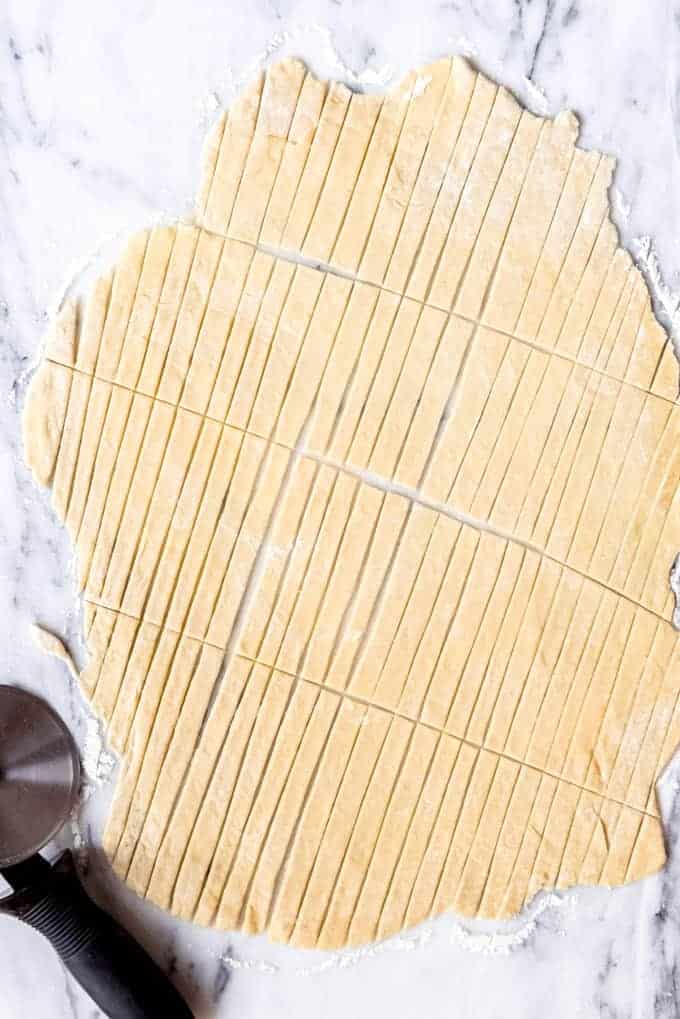 An image of homemade egg noodle dough that has been rolled out and cut into thin strips.