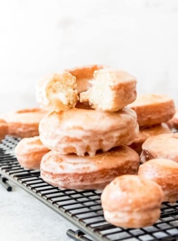 An image of glazed cake doughnuts stacked on top of each other on a wire rack