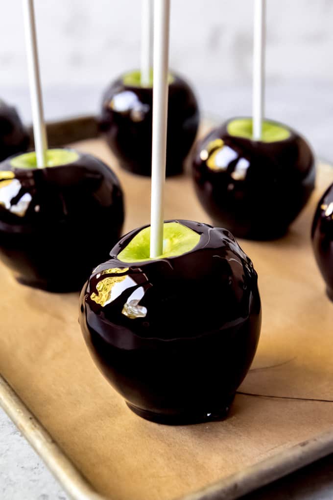 An image of Halloween candied apples setting up on a parchment paper-lined baking sheet.