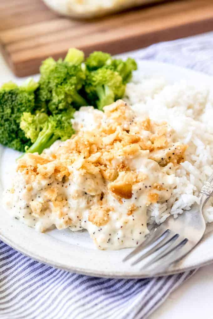 An image of a serving of poppy seed chicken on a plate with rice and broccoli.