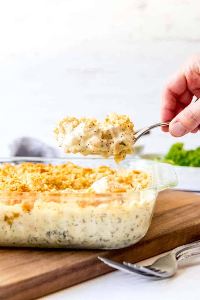 An image of a hand lifting a spoon full of creamy chicken casserole out of the baking dish.