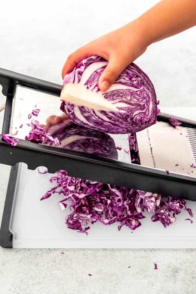 An image of cabbage being shredded on a mandoline.