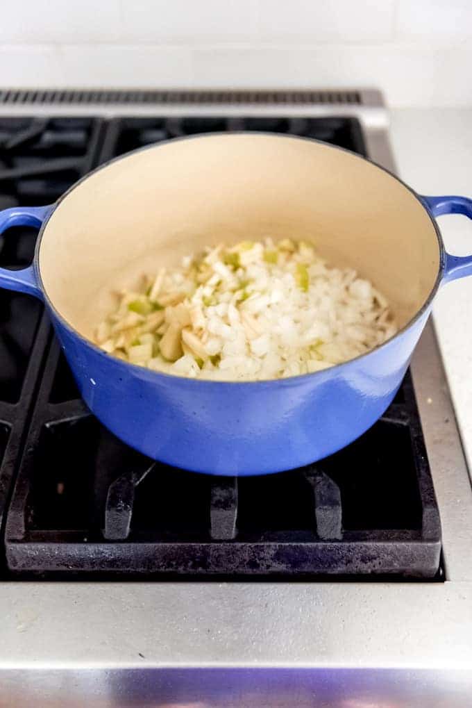 An image of a large dutch oven with apples and onions being sauteed on a stovetop. 
