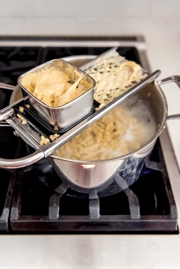 An image of spaetzle batter being dropped into a pot of boiling water.