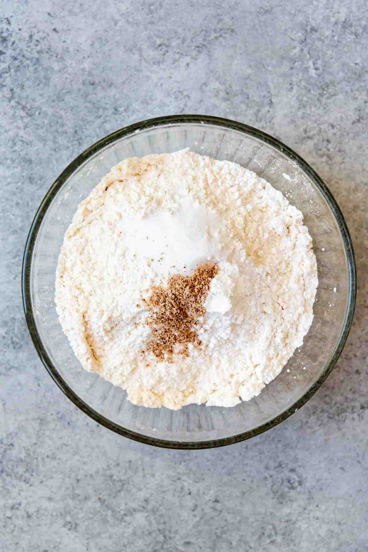 Combining dry ingredients in a mixing bowl with grated nutmeg on top.