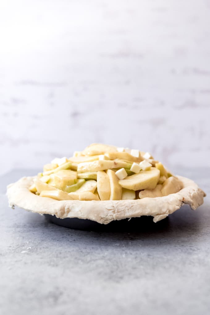 An image showing sliced apples mounded in the center of a pie crust and dotted with butter.