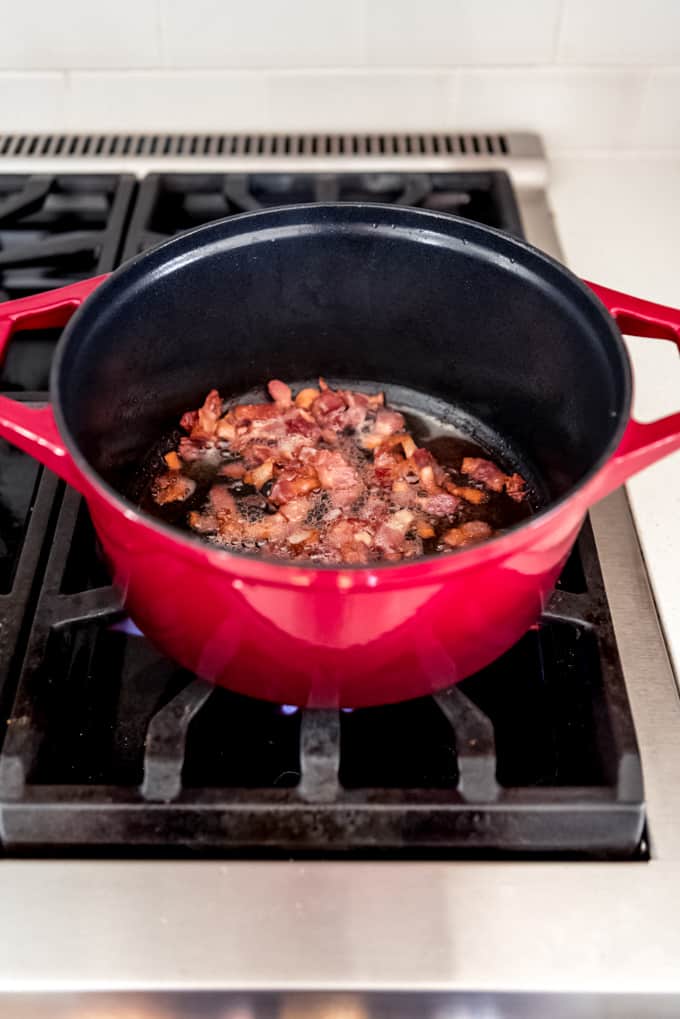 An image of chopped bacon frying in a dutch oven.