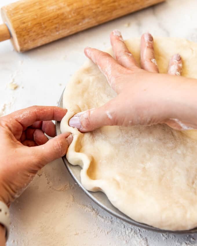 Fingers being used to pinch pie crust into a crimped edge.