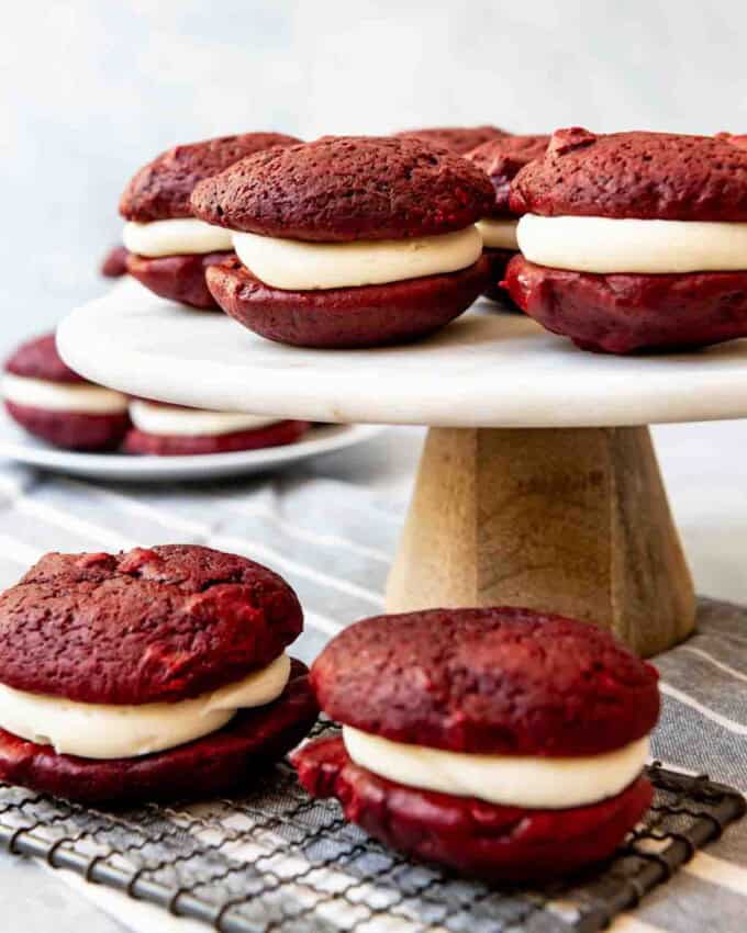 An image of red velvet whoopie pies on a cake stand and wire cooling rack.