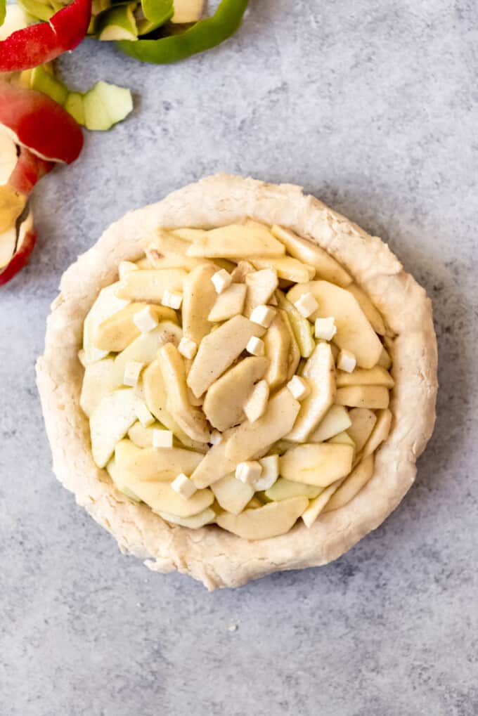 Adding apple pie filling to a pastry crust and dotting with butter.