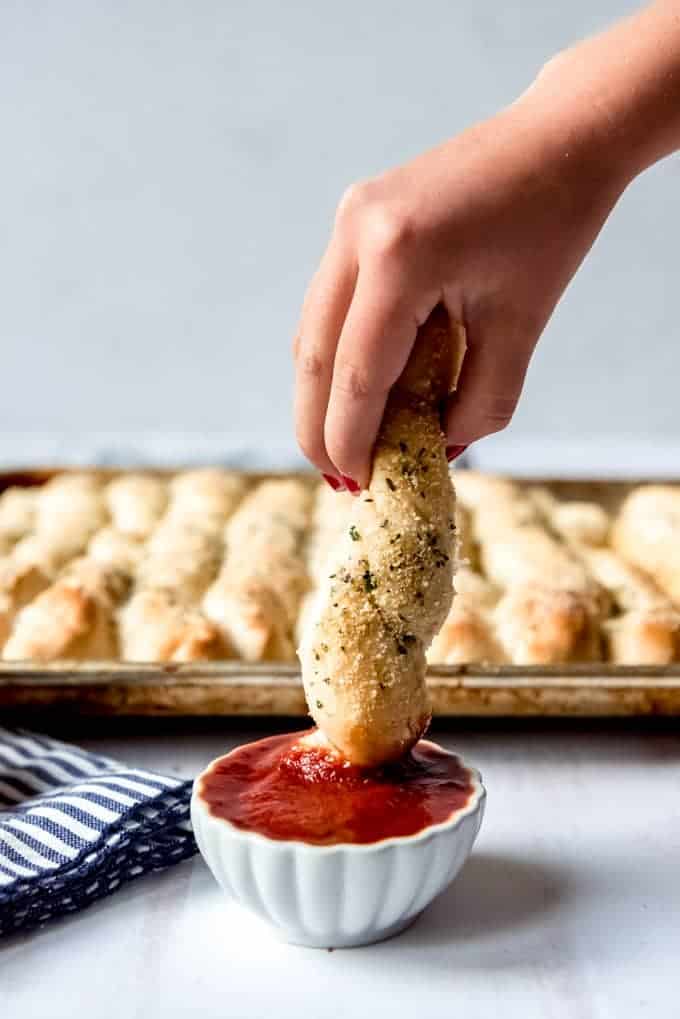 An image of a soft breadstick being dunked in marinara sauce.
