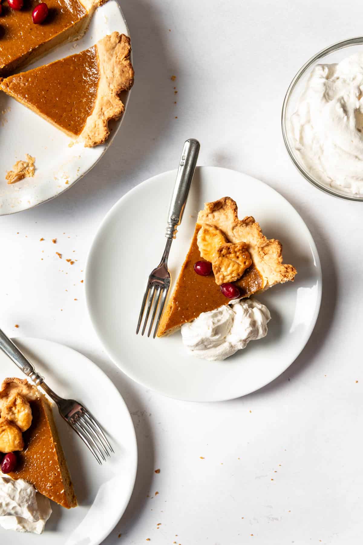 An overhead image of slices of pumpkin pie on plates with whipped cream.