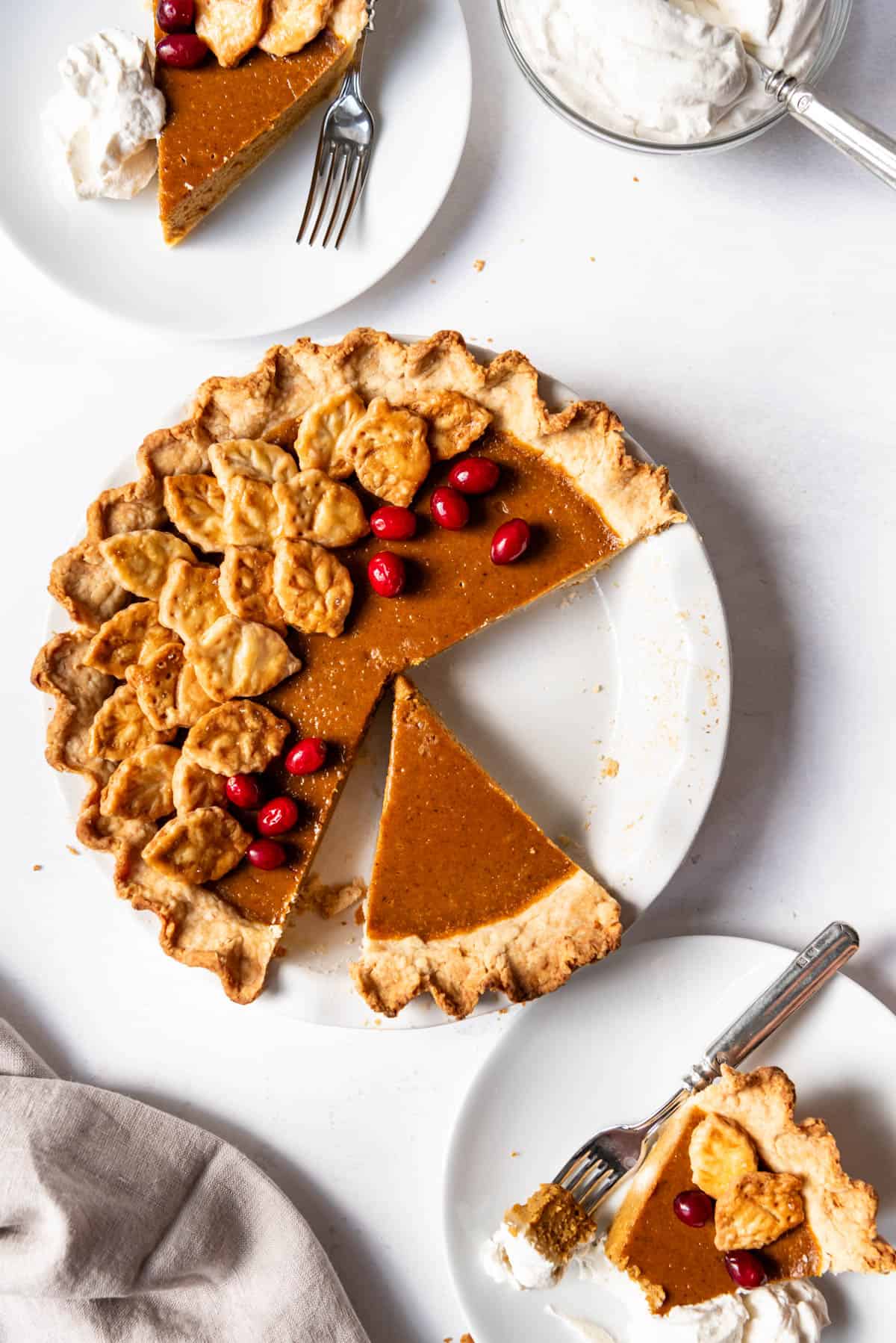 An image of a pumpkin pie with slices cut out of it and cranberries decorating the top.