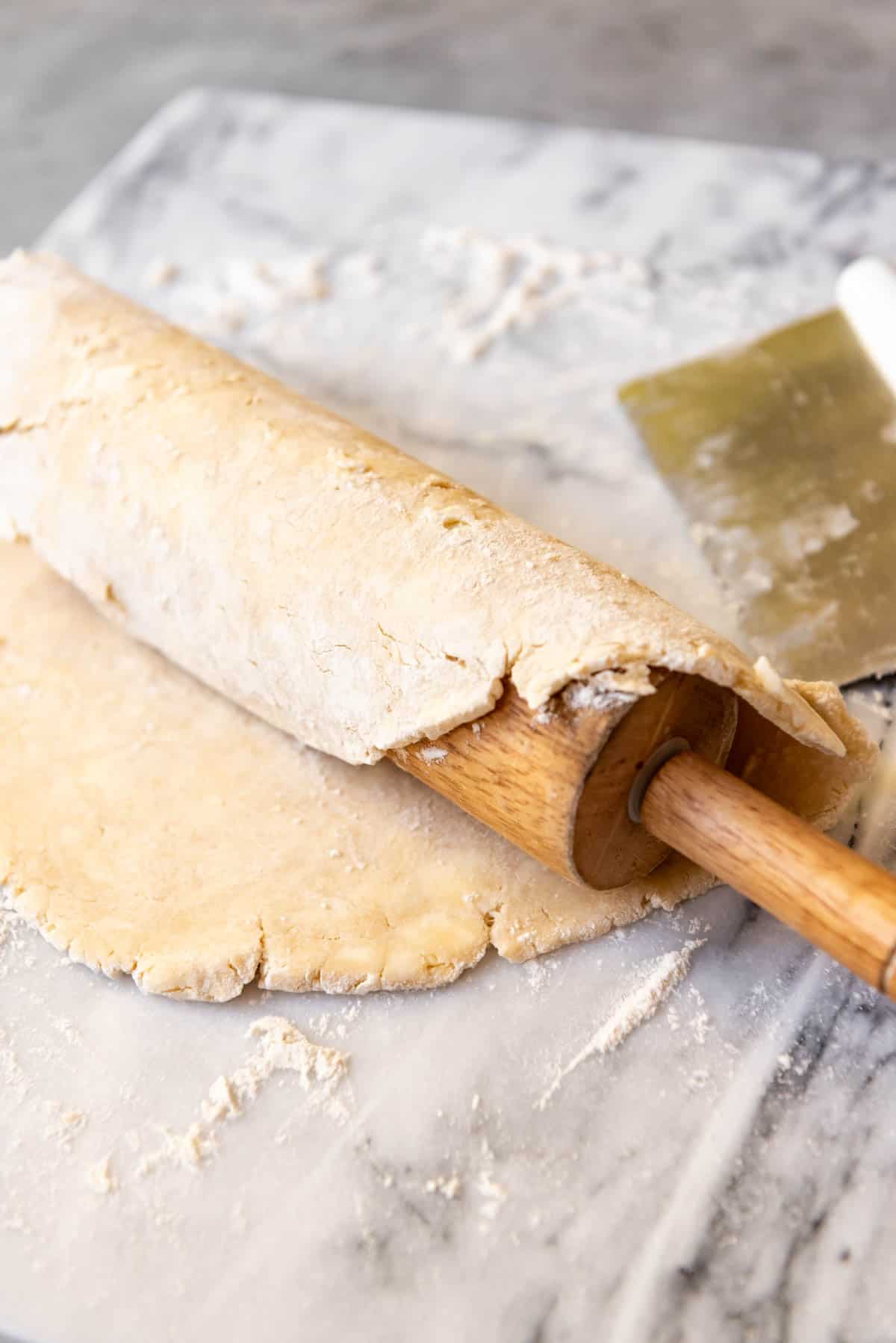 An image of an unbaked pie crust rolled onto a rolling pin to transfer to a pie plate.