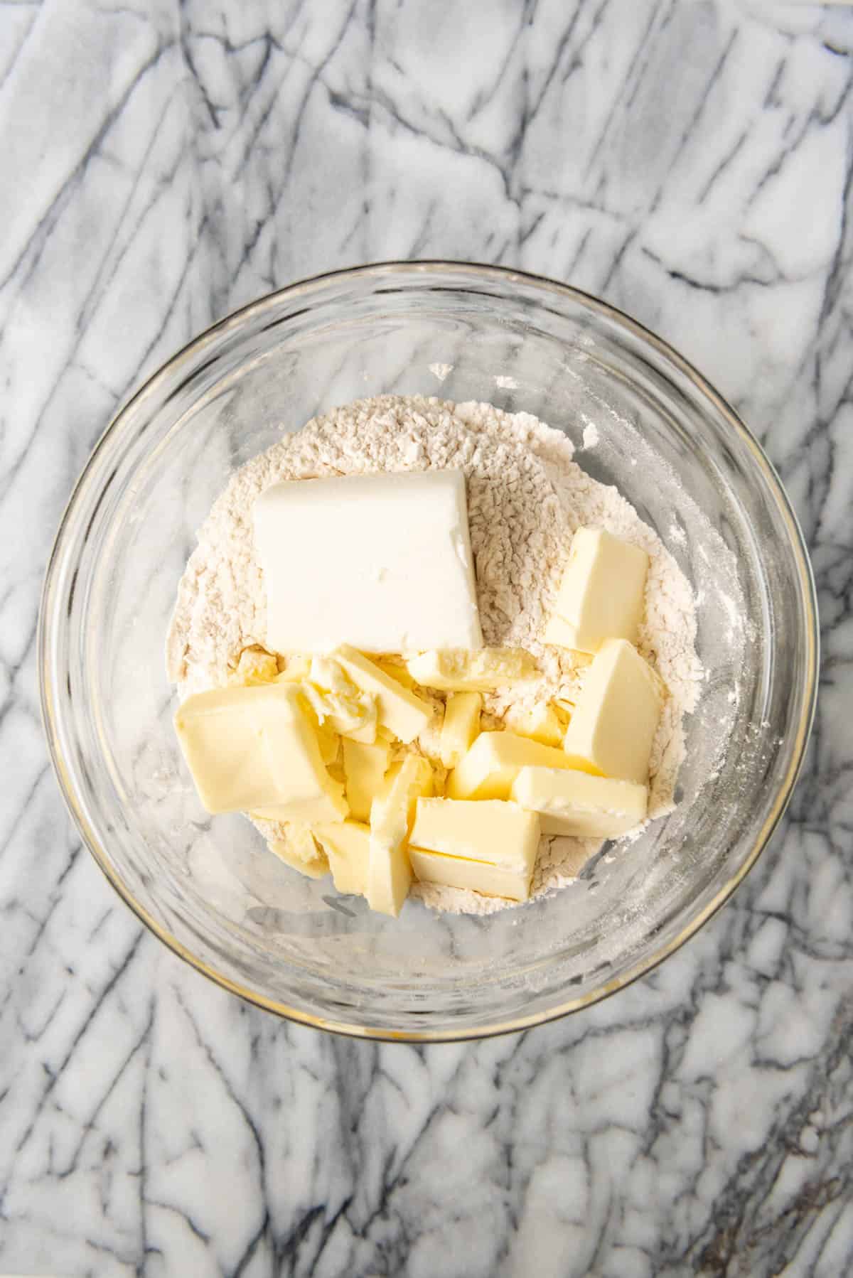 Adding shortening and salted butter to flour and salt in a mixing bowl.