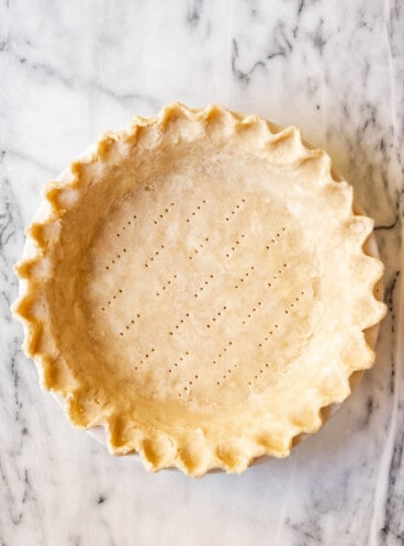 An image of an unbaked pie crust with fork marks on the bottom to blind bake the crust.