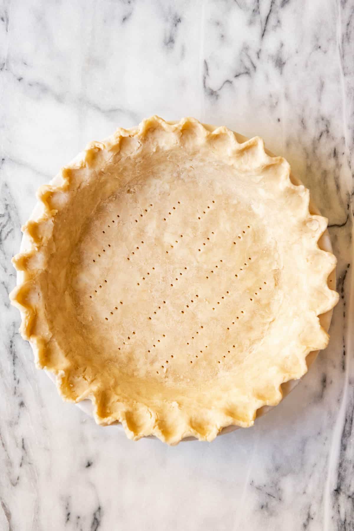 An image of an unbaked pie crust with fork marks on the bottom to blind bake the crust.