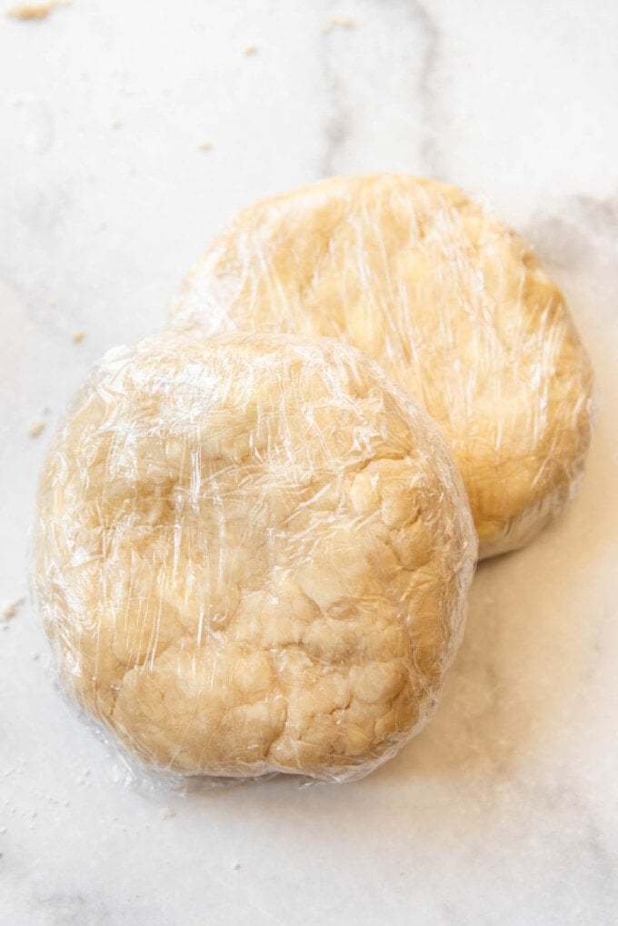 Two discs of pie crust wrapped in plastic wrap.