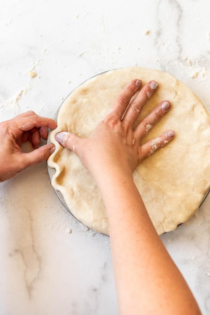 Hands crimping a top pie crust by pinching the thumb between the index finger and thumb on the opposite hand.