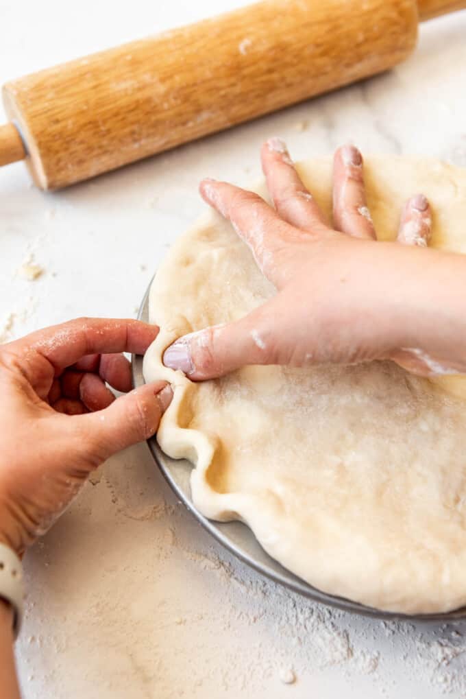 Fingers pinching pie crust into a crimp.