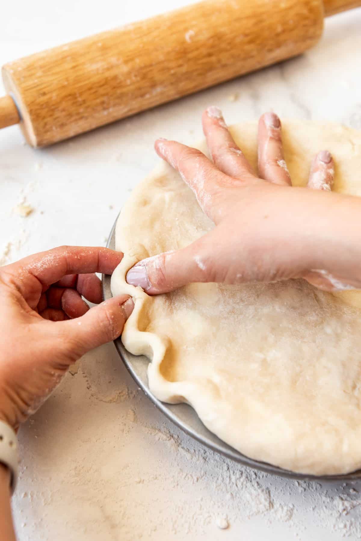 Fingers pinching pie crust into a crimp.