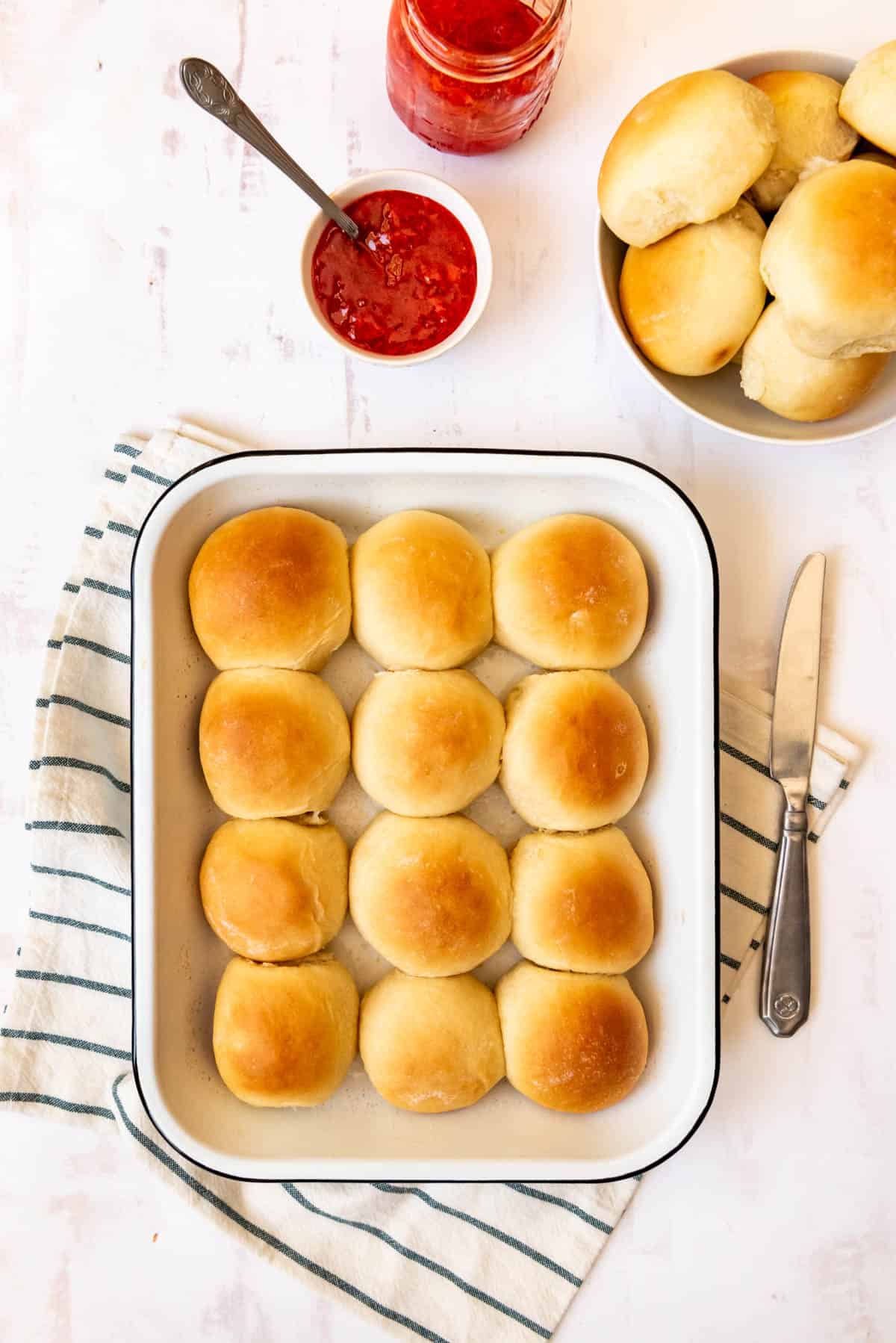 An image of homemade potato rolls in a baking dish with strawberry jam in a bowl next to them.