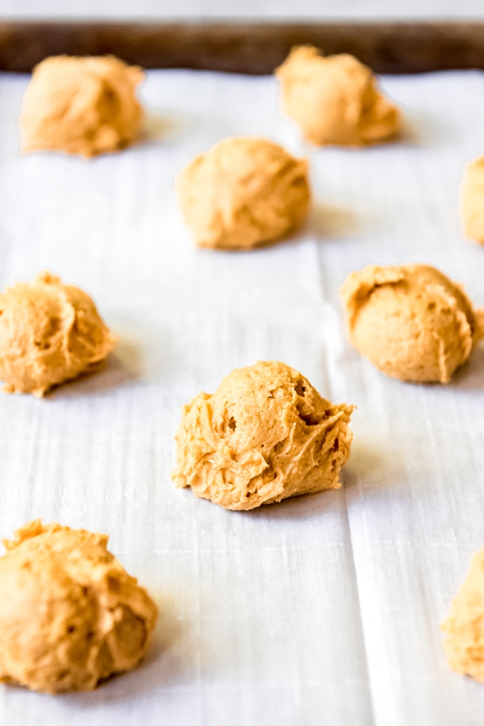 Dropping spoonfuls of pumpkin cookie dough onto a parchment lined baking sheet.