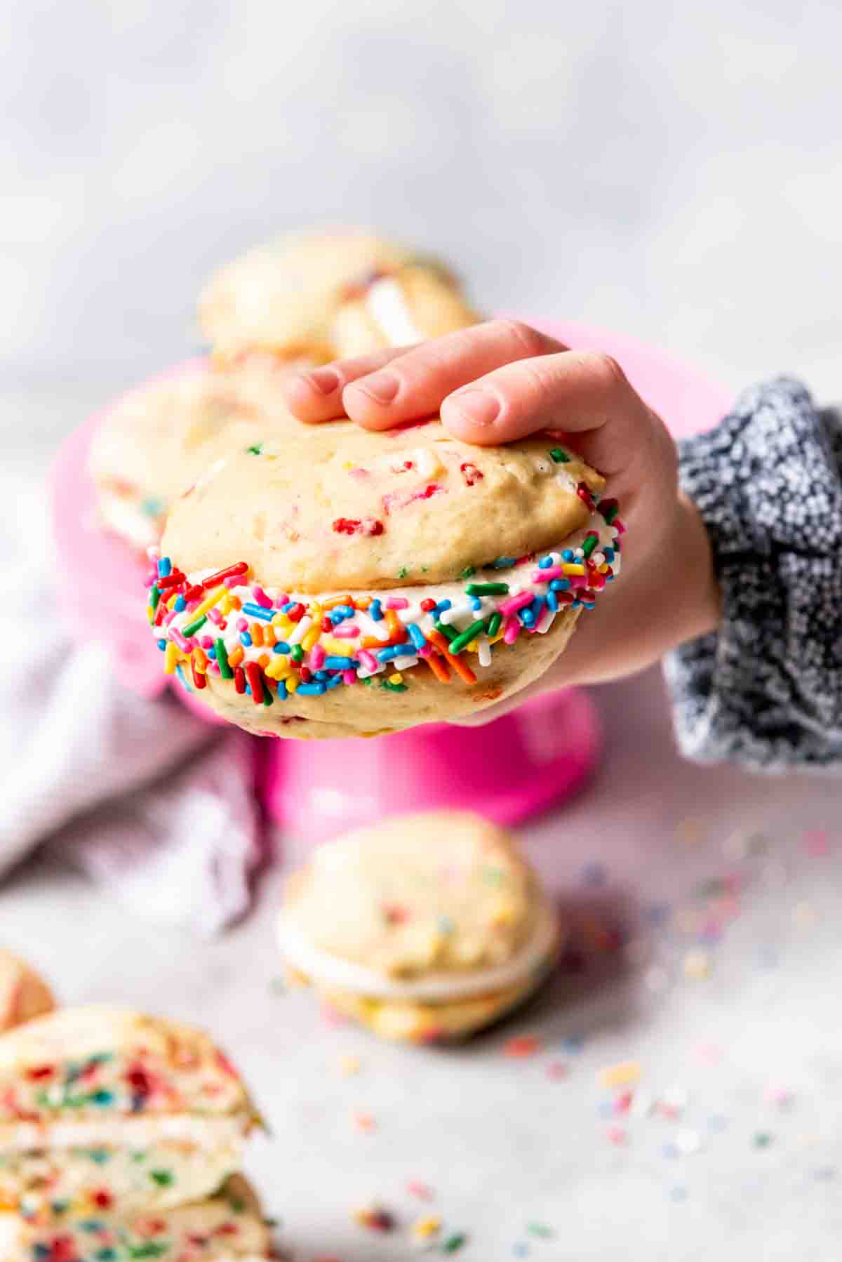 An image of a hand holding a funfetti whoopie pie with sprinkles around the edges.