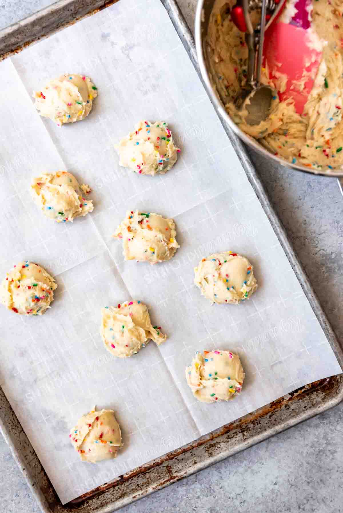 An image of funfetti cookie batter on a parchment-lined baking sheet.