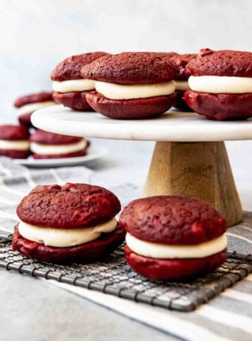 An image of red velvet whoppie pies on a cake stand and wire cooling rack.