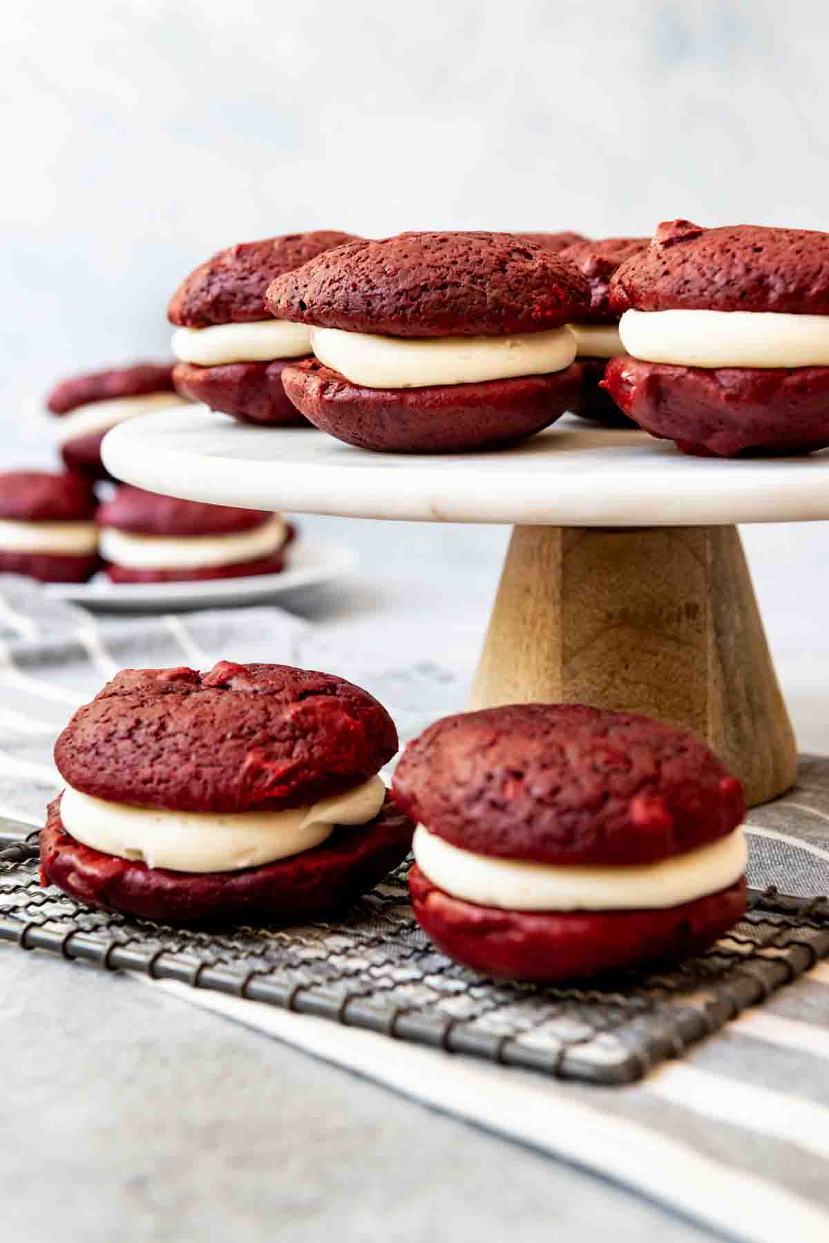 An image of red velvet whoppie pies on a cake stand and wire cooling rack.