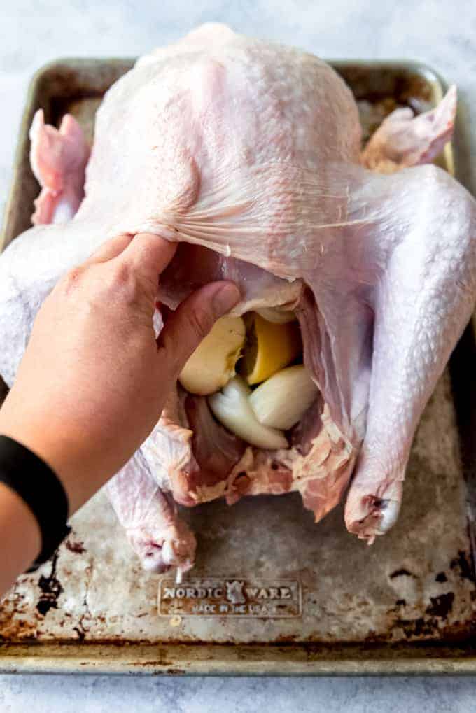 An image of a hand loosening the turkey skin from the turkey meat on a whole turkey.