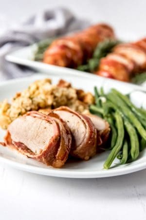 An image of a sliced pork tenderloin on a plate with green beans and cornbread dressing.