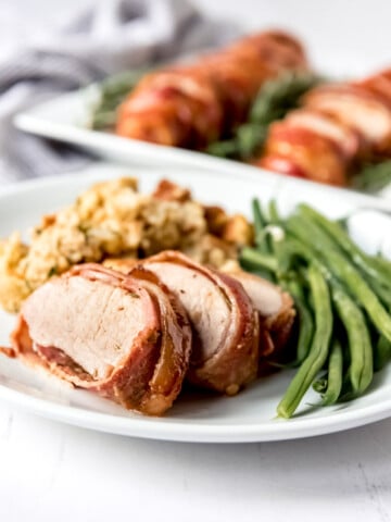 An image of a sliced pork tenderloin on a plate with green beans and cornbread dressing.