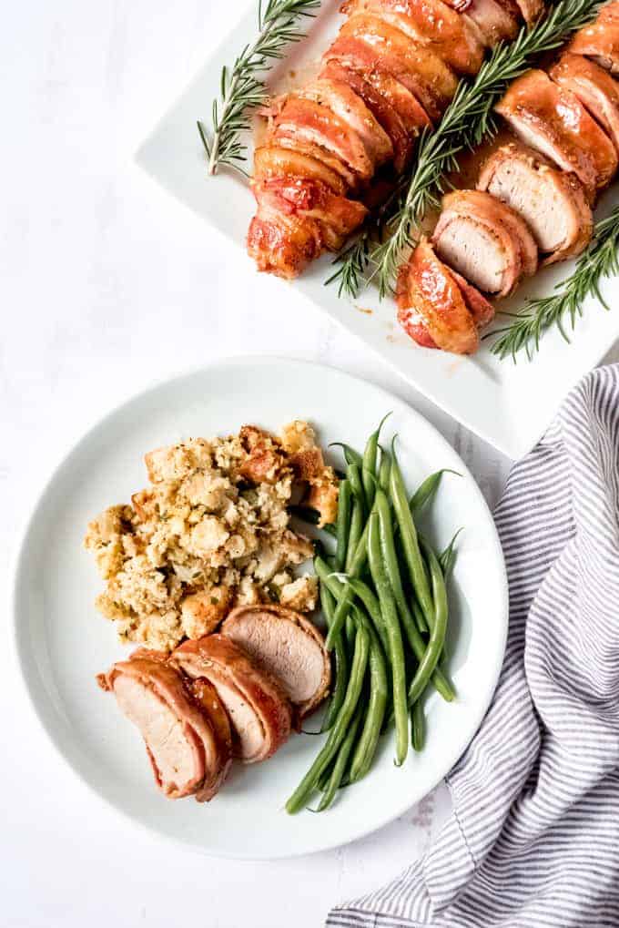An image of a a sliced pork tenderloin on a white plate with cornbread stuffing and green beans.
