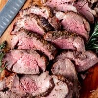 An image of a sliced garlic herb butter beef tenderloin roast on a cutting board.