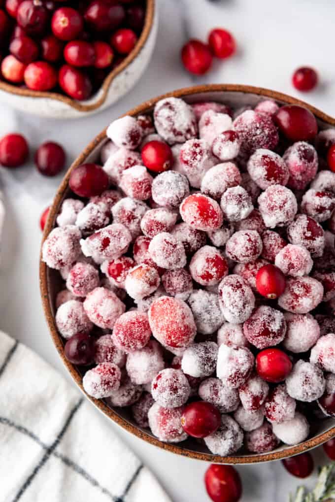 A bowl of sparkling sugared cranberries next to fresh cranberries.