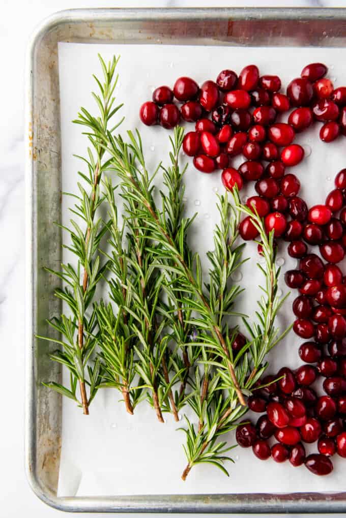 Rosemary and cranberries on a baking sheet lined with parchment paper.