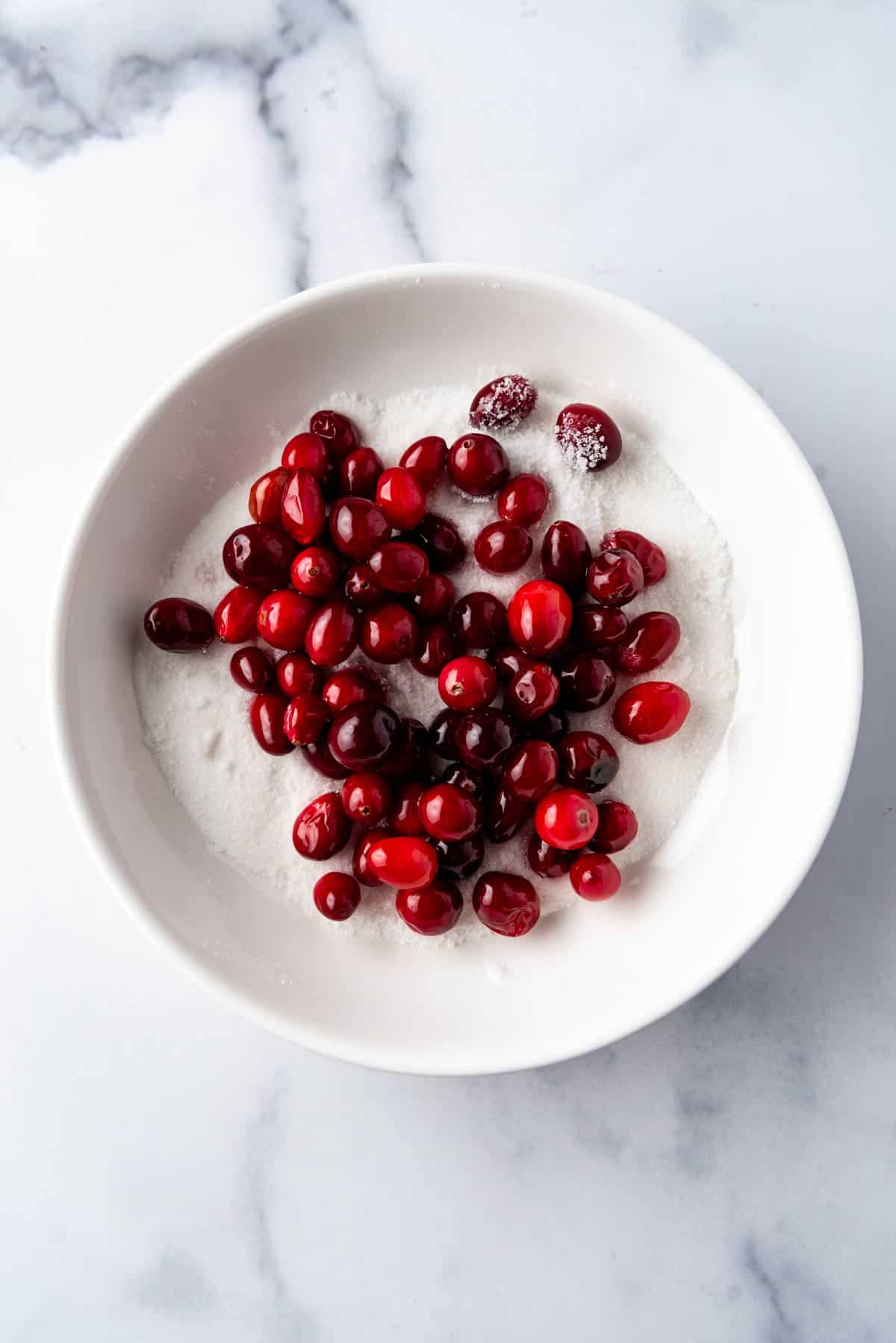 Sticky cranberries being added to a bowl of granulated sugar.