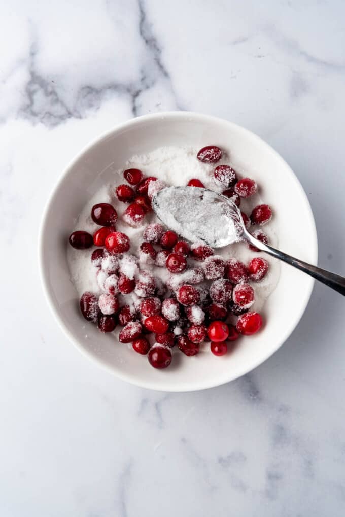 Tossing soaked sugared cranberries in granulated sugar in a white bowl.
