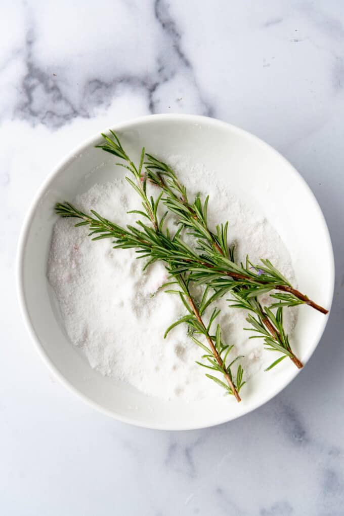 Adding rosemary sprigs to a bowl of granulated sugar.