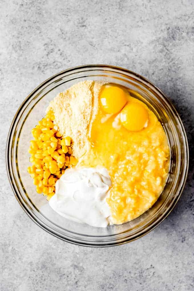 An image of a mixing bowl filled with Jiffy corn mix, creamed corn, sour cream, canned corn kernels, butter, and eggs.