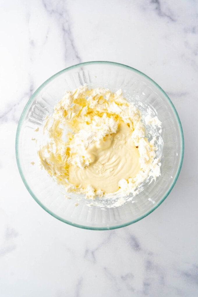 Adding melted white chocolate to cream cheese in a bowl.