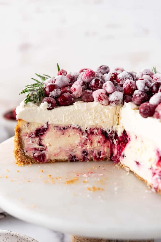 A side angle view of a cranberry cheesecake with a few slices removed.