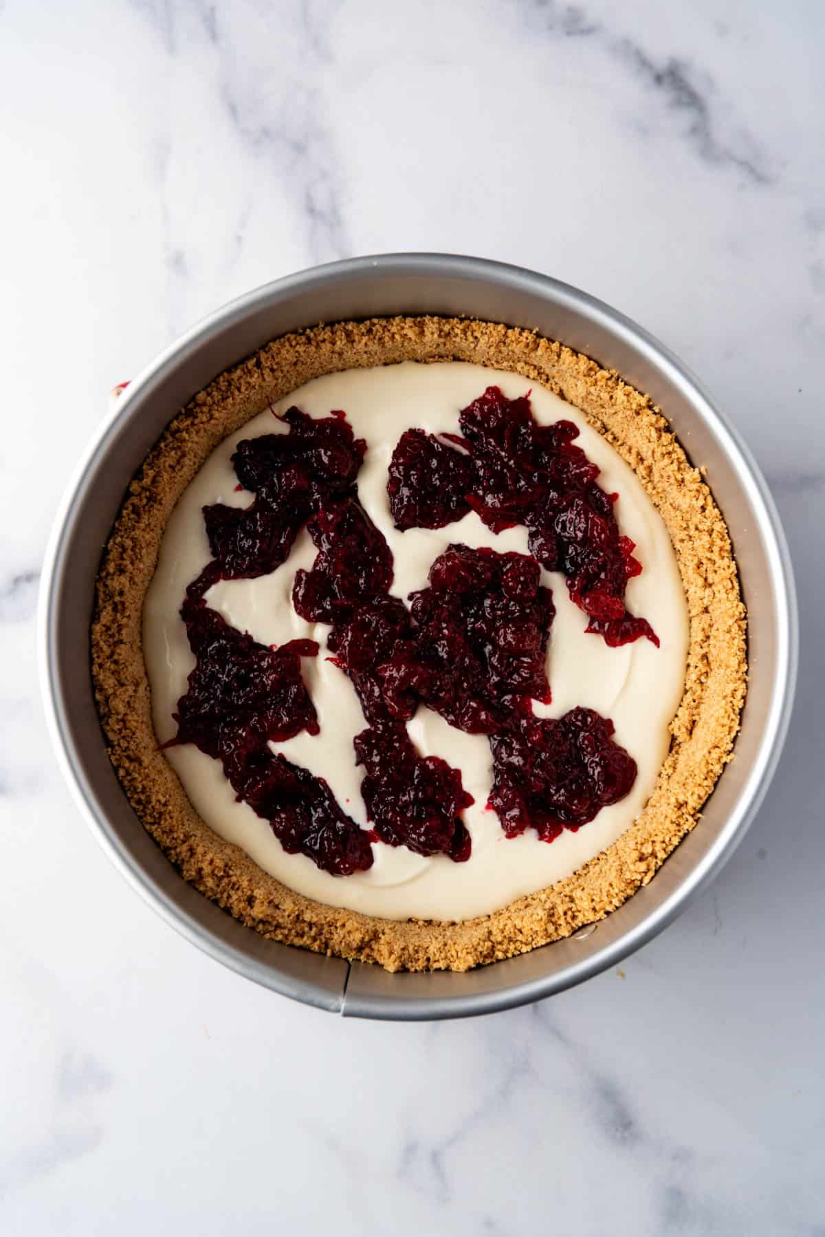 Adding dollops of cranberry sauce to cheesecake batter in a graham cracker crust.